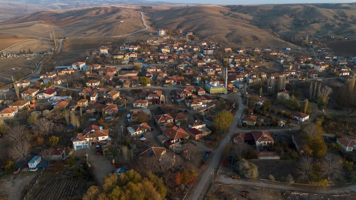 Aerial view of a traditional Turkish village surrounded by hills, showing red-roofed houses, narrow streets, and rural landscape in autumn