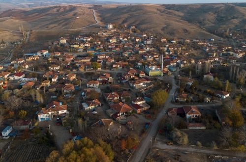 Aerial view of a traditional Turkish village surrounded by hills, showing red-roofed houses, narrow streets, and rural landscape in autumn